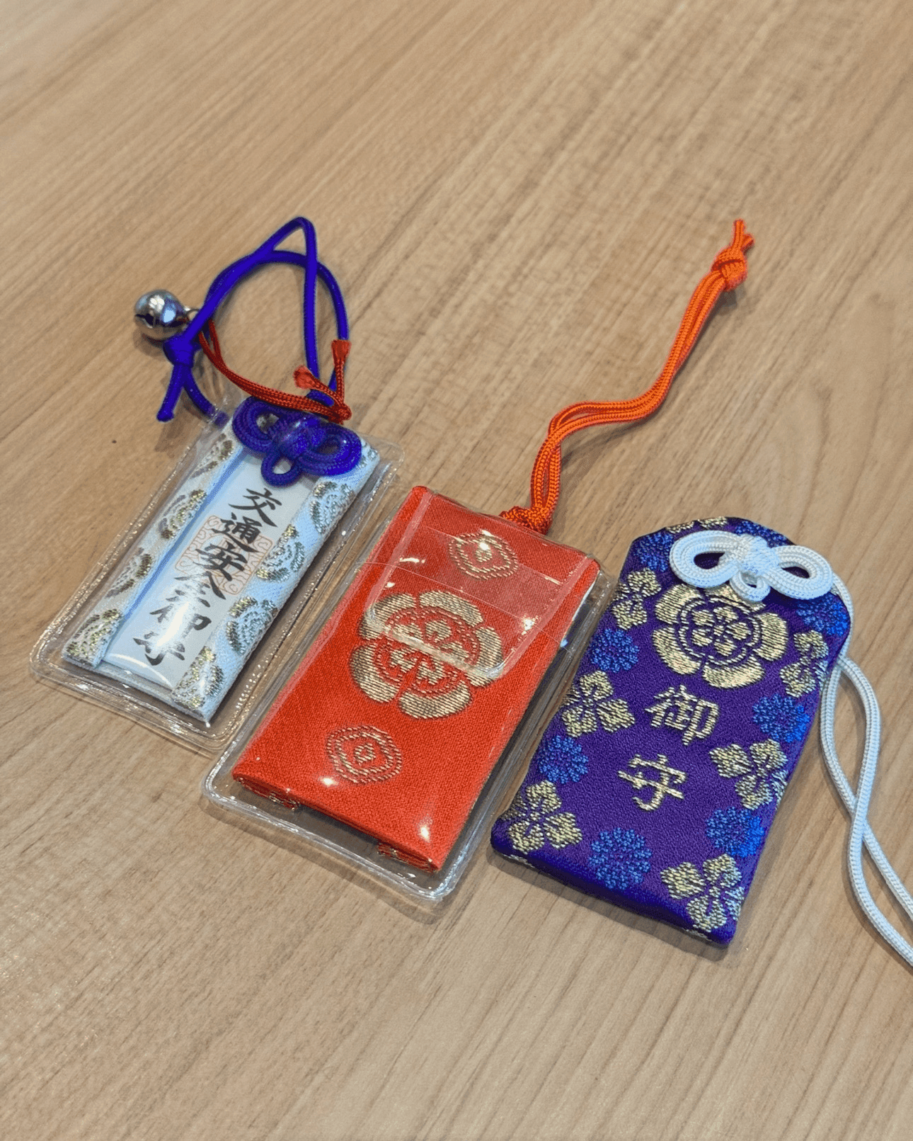 Tres coloridos amuletos omamori japoneses, que se cree que traen suerte y protección, expuestos sobre madera.
